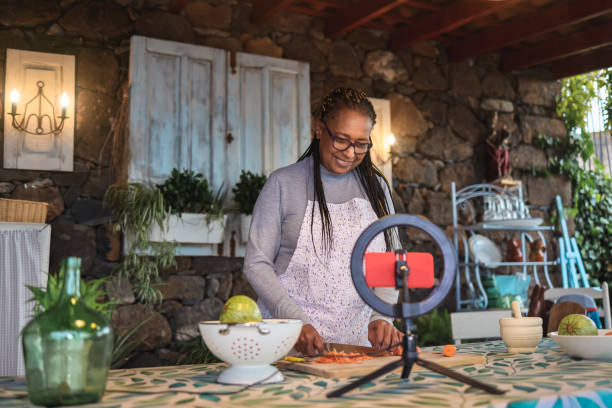 African senior woman streaming online virtual masterclass cooking lesson outdoors at home - Focus on face