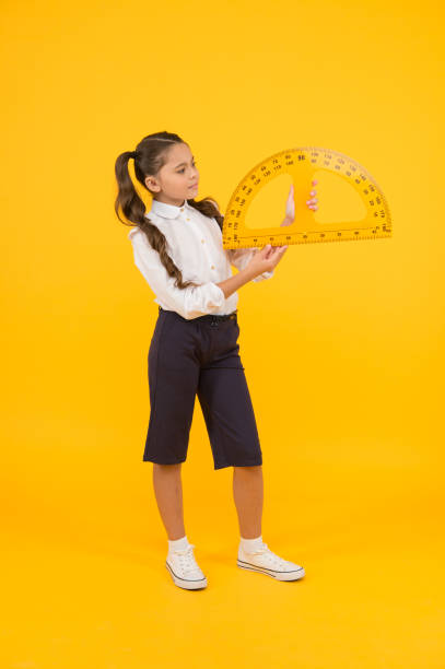istock Setting square with protractor. Little girl using triangle to measure angles in degrees on yellow background. Small child holding school protractor for geometry lesson. Learning to use protractor 1297591053
