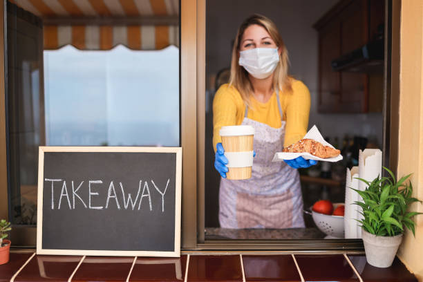istock Young woman preparing takeaway breakfast and coffee inside bakery shop while wearing safety mask - Focus on food 1297592395