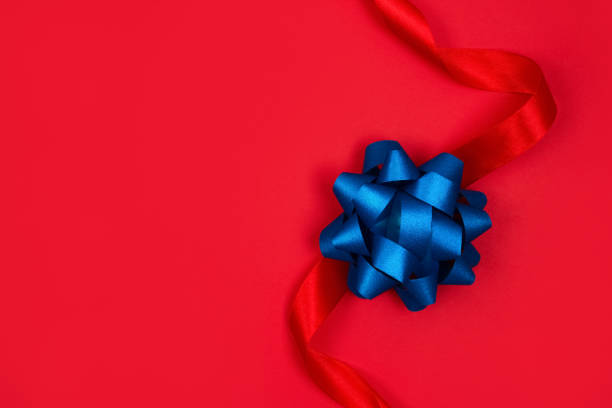istock Top view on decorative blue ribbon bow on red background with copy space for text. Giving presents concept. Festive composition for greeting card or holidays sale background. Selective focus 1297593379