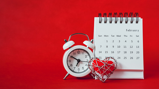 white calendar of February month ,red heart in wire mesh and analog clock on grunge red paper background , panorama, Valentine  background , dating on valentine's day concept