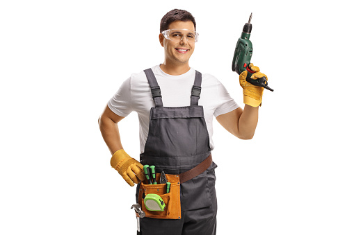 Repairman with protective goggles and a tool belt holding a drill isolated on white background