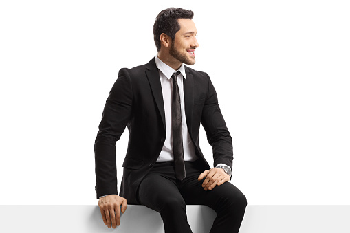 Young handsome man in a suit sitting on a panel isolated on white background