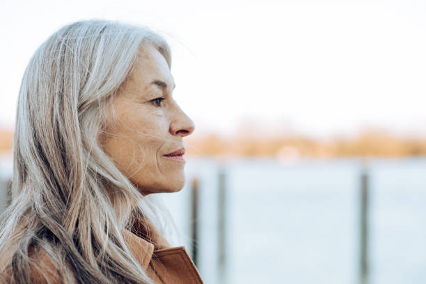 Headshot of a thoughtful mature woman looking at the distance Portrait of a thoughtful mature woman standing on the beach and looking at the distance. mourner photos stock pictures, royalty-free photos & images