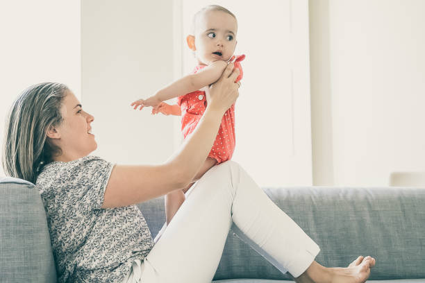 istock Pretty mother sitting on sofa and holding her little daughter 1297599596