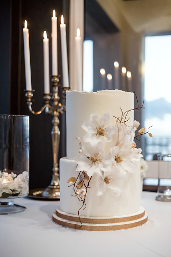 White wedding cake decorated with flowers and candles in the background