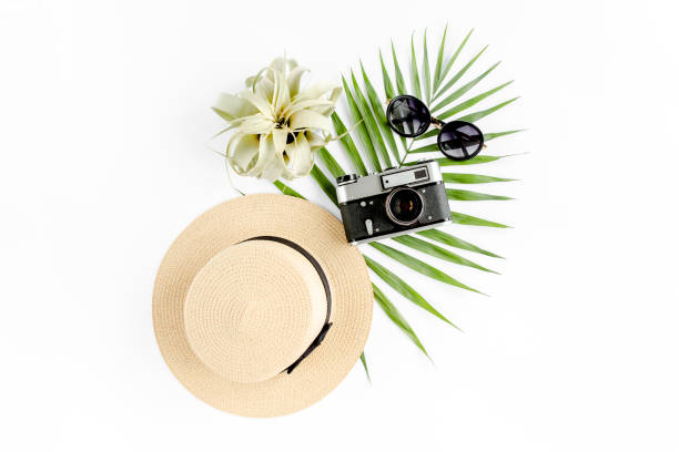 istock Flat lay traveler accessories on white background with retro camera, straw hat, sunglasses, and tropical palm leaf. Travel concept background 1297600614