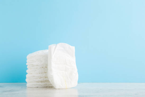 istock Stack of white soft new baby diapers on wooden table at light blue wall background. Pastel color. Closeup. Empty place for text or logo. Front view. 1297600916
