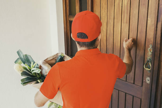 istock Back view of courier knocking at door and holding vegetables 1297600956