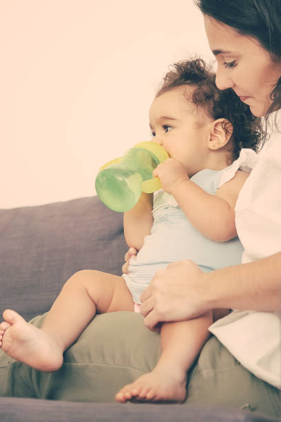 istock Cute baby sitting on moms lap and drinking water 1297602312