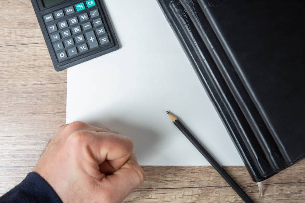 istock Stack of personal leather bounded journals. Black pencil on empty paper blank. Man`s arm and calculator. Wooden table background. Close-up. 1297602640