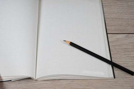 Black pencil on empty opened notebook. Wooden table background.
