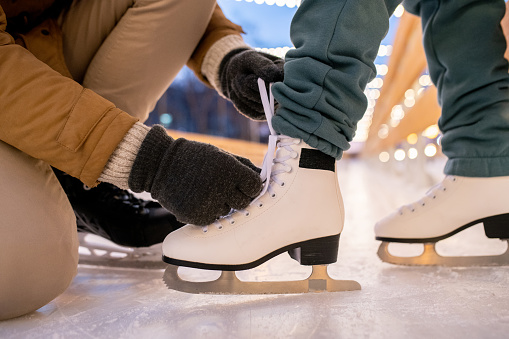 Close-up of man tying shoelace on skates of his girlfriend while they standing on skating rink