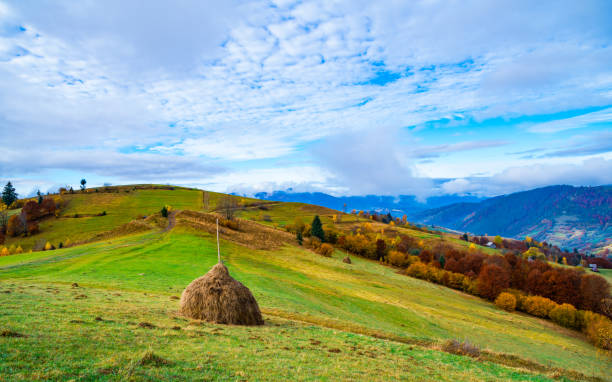 View of scenic landscape with bright colorful sky over foggy mountains. Majestic sunrise in misty morning valley with haystack on grassland hill. Concept of nature.