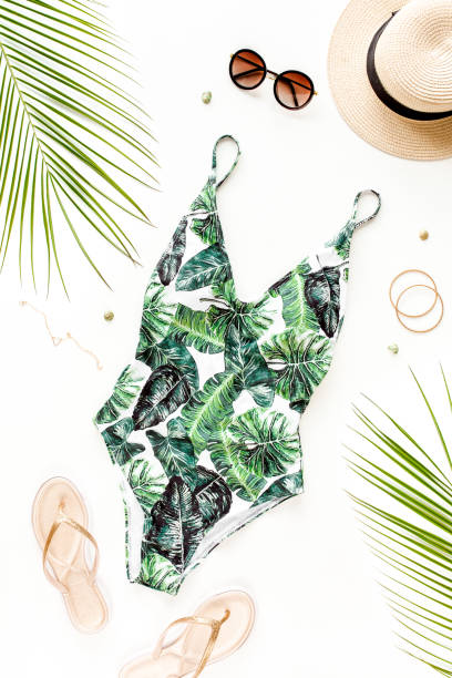 istock Woman's beach accessories: swimsuit with tropical print, straw hat on white background. Summer background 1297606682
