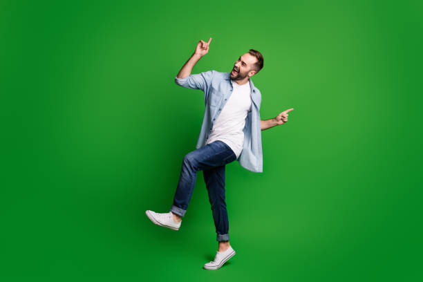 녹색 색상 배경에 고립 된 블루 셔츠 청바지 신발을 입고 춤을 추는 낙관적 인 남자의 풀 사이즈 프로필 사진 - 춤 뉴스 사진 이미지