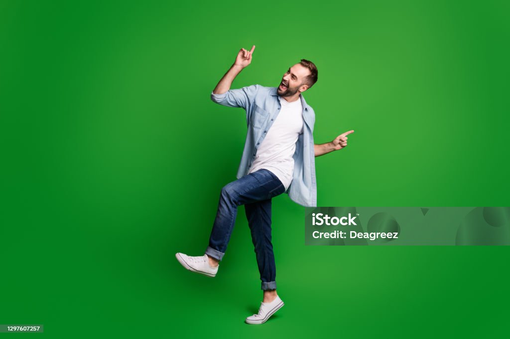 Full size profile photo of optimistic guy dancing wear blue shirt jeans footwear isolated on green color background Full size profile photo of optimistic guy dancing wear blue shirt jeans footwear isolated on green color background. Dancing Stock Photo