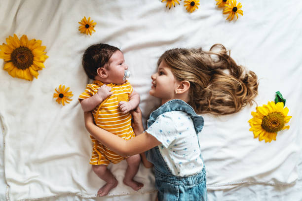 menina deitada na cama ao lado de seu irmão mais novo, cercada de girassóis - newborn little girls baby lying down - fotografias e filmes do acervo