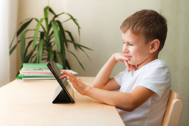 istock Cute boy sittingwith tablet at desk. Child using gadgets for study and play. 1297607750