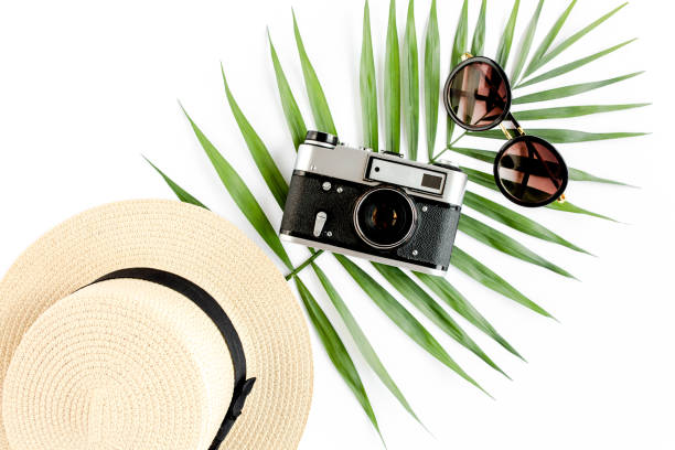 istock Flat lay traveler accessories on white background with retro camera, straw hat, sunglasses, and tropical palm leaf. Travel concept background 1297609913