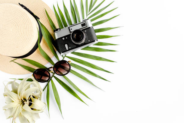 istock Flat lay traveler accessories on white background with retro camera, straw hat, sunglasses, and tropical palm leaf. Travel concept background 1297610191
