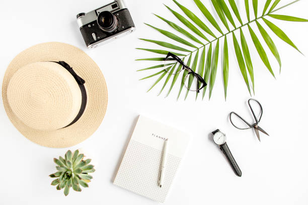 istock Top view home office desk. Workspace with straw hat, glasses, retro camera, notepad and tropical palm leaf on white background. Flat lay, top view 1297611338