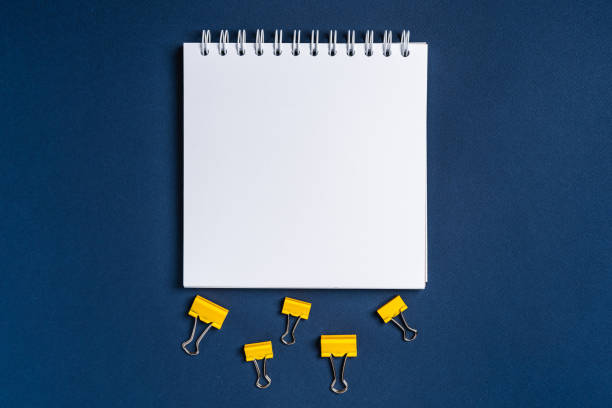 istock Blank notepad on dark blue background and stationery clips, minimalism concept 1297611631