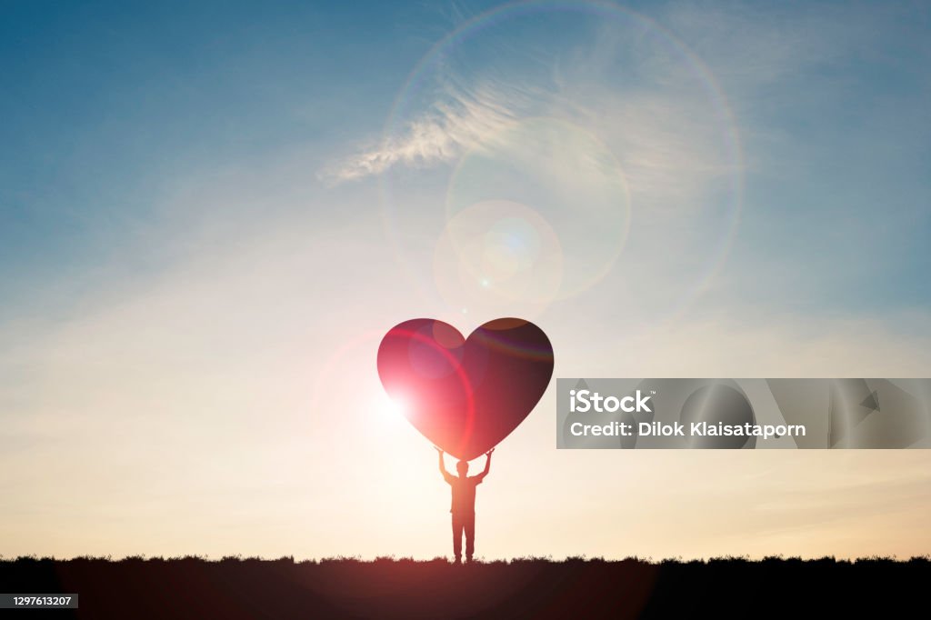 Silhouette man show two hand rise up and carrying heart with sunlight  and blue sky , Valentine 's day concept. Charity Benefit Stock Photo
