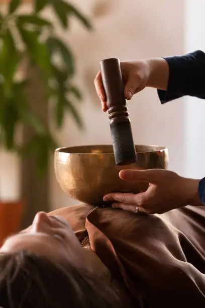 Woman making relaxing massage, meditation, sound therapy with tibetian singing bowls. Stress relief. Selective focus. Bottom view.