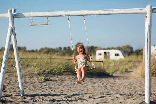 Portrait of a happy young Caucasian little girl using a swing set at the beach, playing and having fun on a vacation