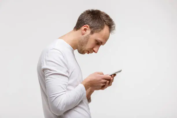 Close up portrait of man looking and using smart phone with scoliosis, side view, isolated on gray background. Rachiocampsis, kyphosis curvature of neck, Incorrect posture,
orthopedics concept