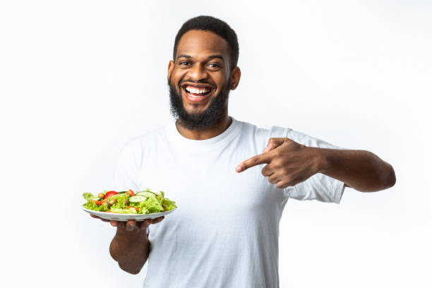 istock Cheerful Black Guy Pointing Finger At Salad Over White Background 1297622953