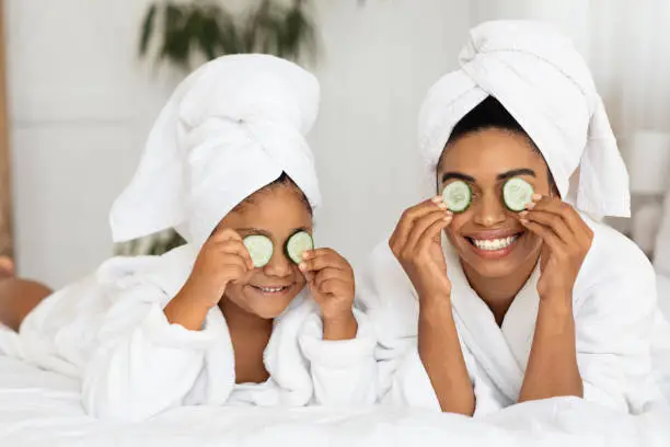 Photo of Funny Black Mom And Daughter In Bathrobes With Cucumber Slices On Eyes