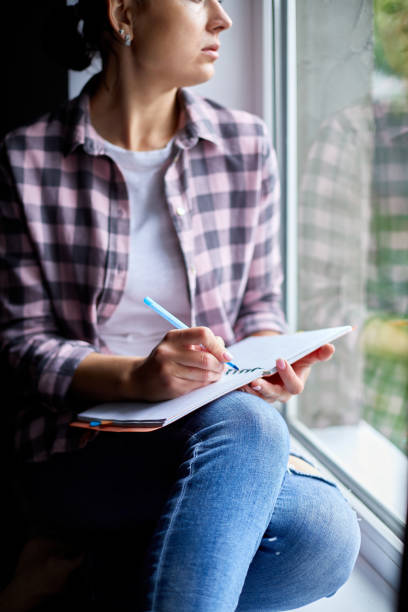 istock Woman, sitting at window at home, writes in notebook goals 1297623196