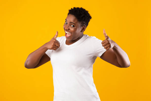 istock Plus-Size Black Lady Gesturing Thumbs-Up With Both Hands, Yellow Background 1297624512