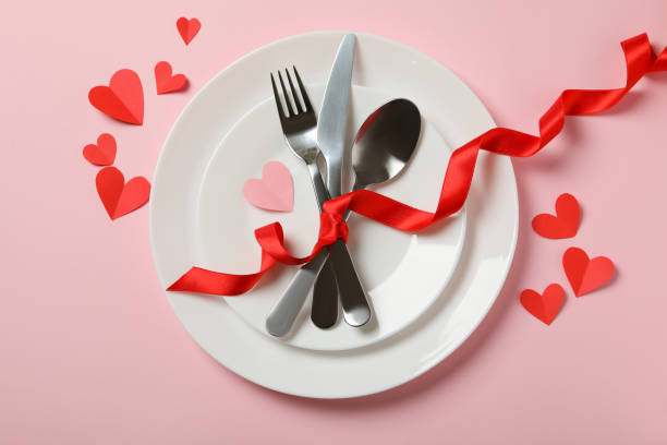 istock Plates with cutlery and red bow on pink background with decorative hearts 1297627364