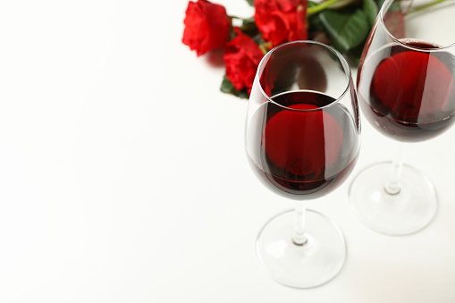 Red roses and glasses of wine on white background, space for text