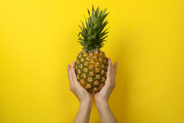 istock Female hands hold ripe pineapple on yellow  background 1297629060