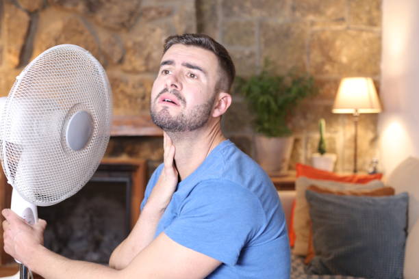hombre durante una ola de calor insoportable con ventilador eléctrico - enfriamiento fotografías e imágenes de stock