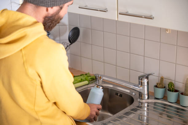 istock Man fills up reusable water bottle in the kitchen 1297630660