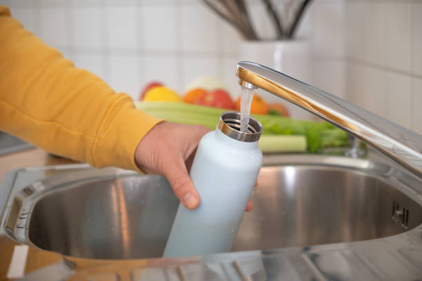 mann füllt wiederverwendbare wasserflasche in der küche - wasserflasche stock-fotos und bilder