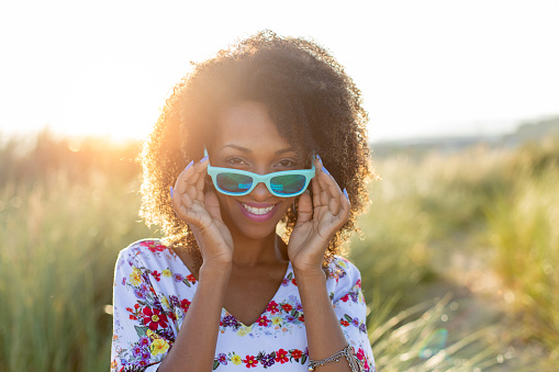 Joyful happy woman on spring or summer outdoor relaxing leisure. Afro hair young black female wearing sunglasses.