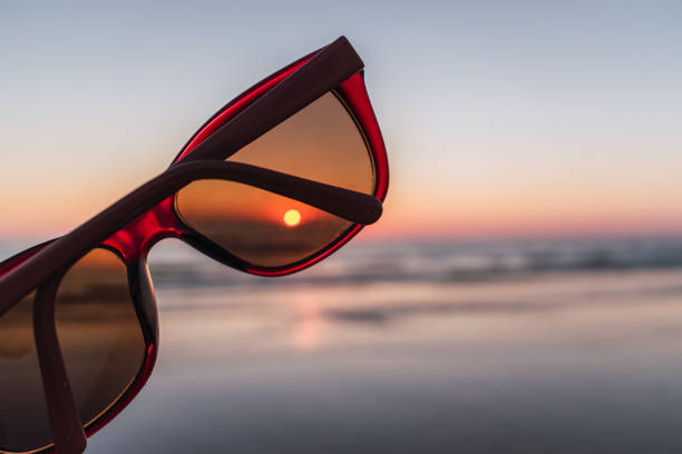 primer plano de gafas de sol rojas en la playa con puesta de sol al fondo - diseño flux fotografías e imágenes de stock