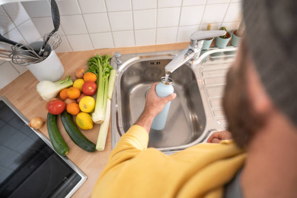 istock Man fills up reusable water bottle in the kitchen 1297631801