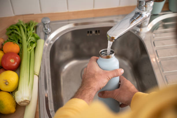 istock Man fills up reusable water bottle in the kitchen 1297631850