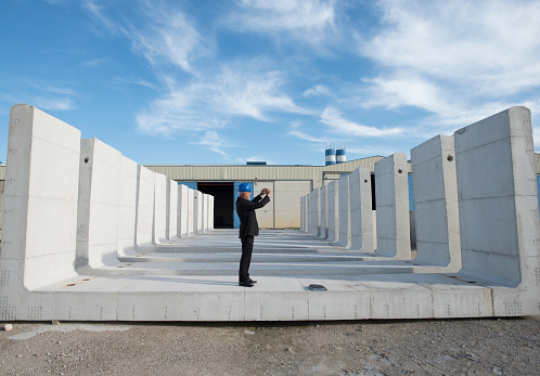 Boss in cement company outdoors takes photograph with phone of concrete structures ready for distribution and intended for prefabricated construction. Cordoba, Spain.