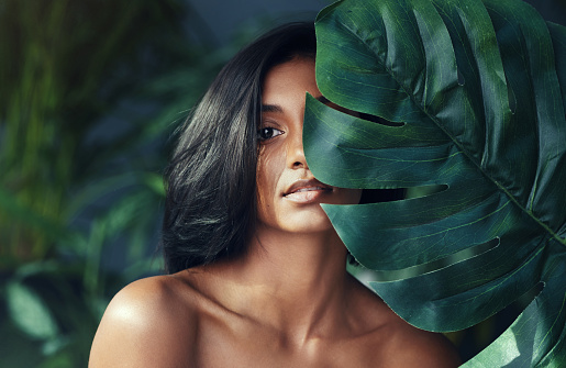 Studio shot of a beautiful young woman holding a monstera leaf against her face