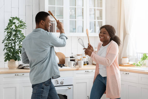 istock Cheerful black couple fighting with kitchenware, playing with utensils tools in kitchen 1297634550