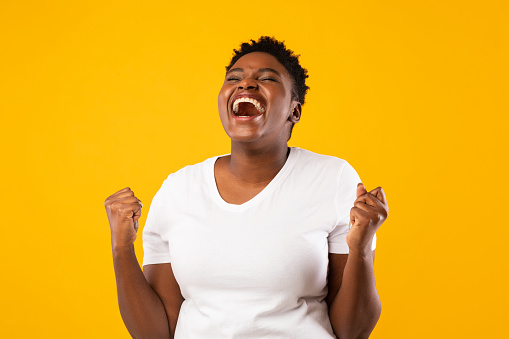 Joy Of Victory. Joyful Oversized Black Woman Shouting Gesturing Yes And Shaking Fists Posing Standing Over Yellow Background, Studio Shot. Excitement And Joy, Success Celebration. Emotional Portrait.