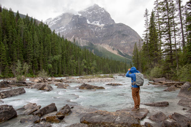 istock Male hiker stands rocks on a glacial river and pulls on hood 1297634591